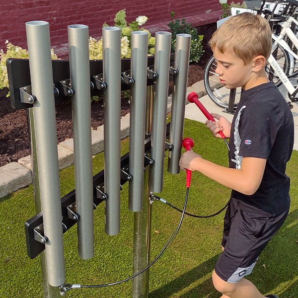 a young boy playing a set of outdoor musical chimes in the music garden at town of versailles