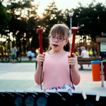 A young girl with downs syndrome playing an outdoor musical instrument with a lady