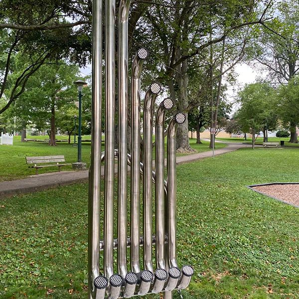 Tall musical pipes on a stand curving up at the bottom that should be hit to produce sounds a music park dedicated to the memory of a young boy named Gavin