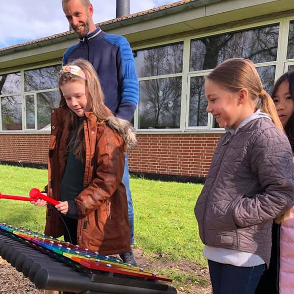 two schoolgirls playing a rainbow coloured outdoor musical instrument in the school playground