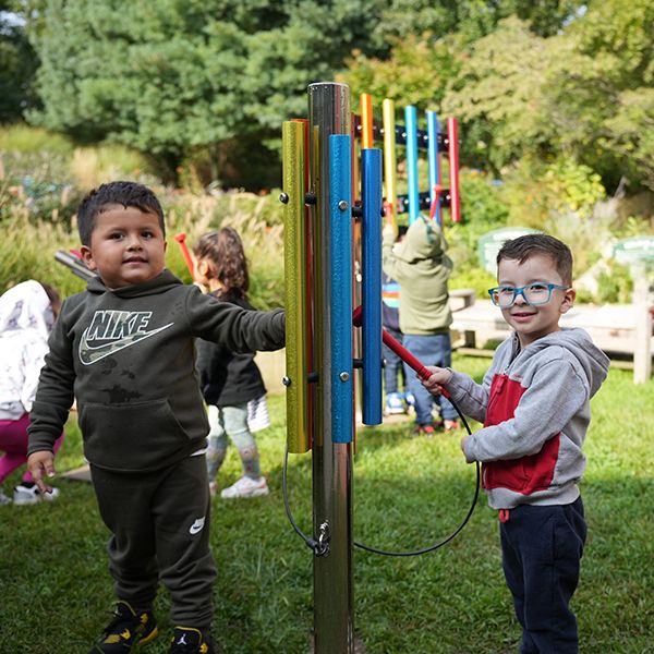 Two young boys playing an outdoor musical chime in a sensory garden