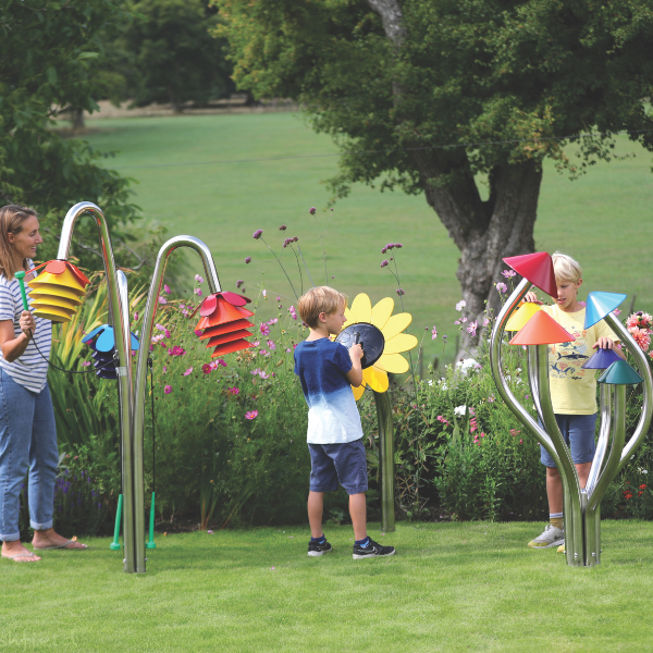 a mother and two boys playing outdoor musical instruments shaped like flowers and mushrooms in a music park