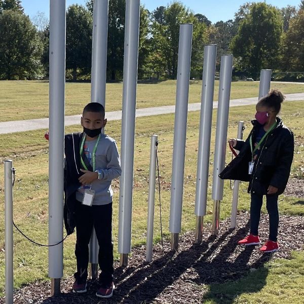 A young boy and girl playing on large tall tubular bells in their school music garden