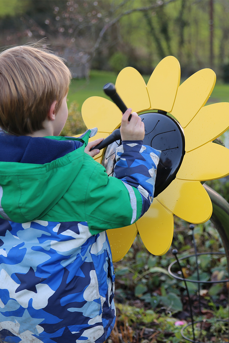 A young boy playing an outdoor musical drum in the shape and colours of a sunflower