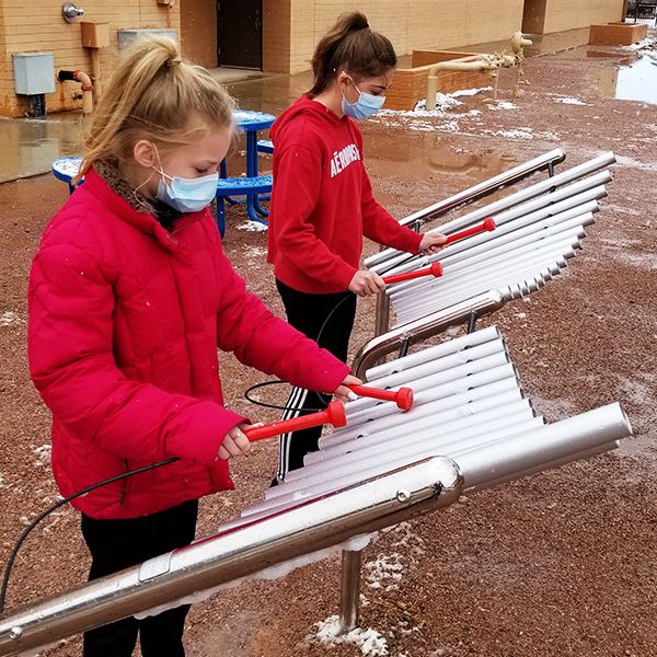 Two schoolgirls wearing a red uniforms playing an outdoor musical instrument in the school playground