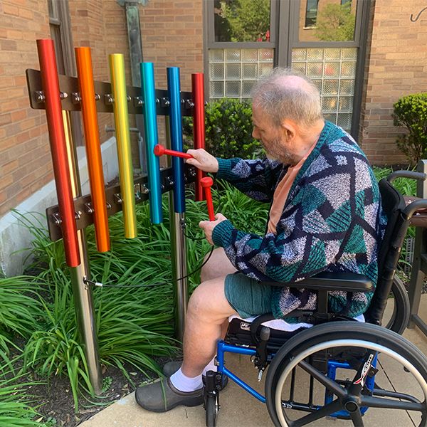 senior male wheelchair user playing a rainbow coloured outdoor chimes in a care home garden