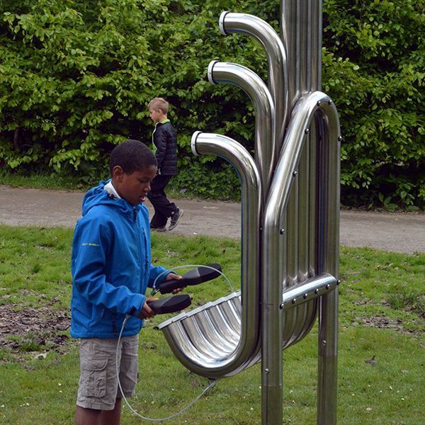 Black boy in a park playing huge silver outdoor musical instrument