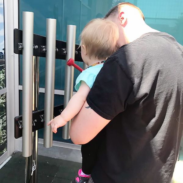 a father holding his baby up and playing musical chimes at the santa maria discovery museum