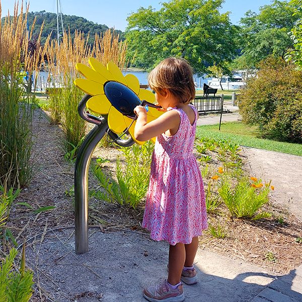 back of a young girl playing an outdoor musical drum shaped like a sunflower