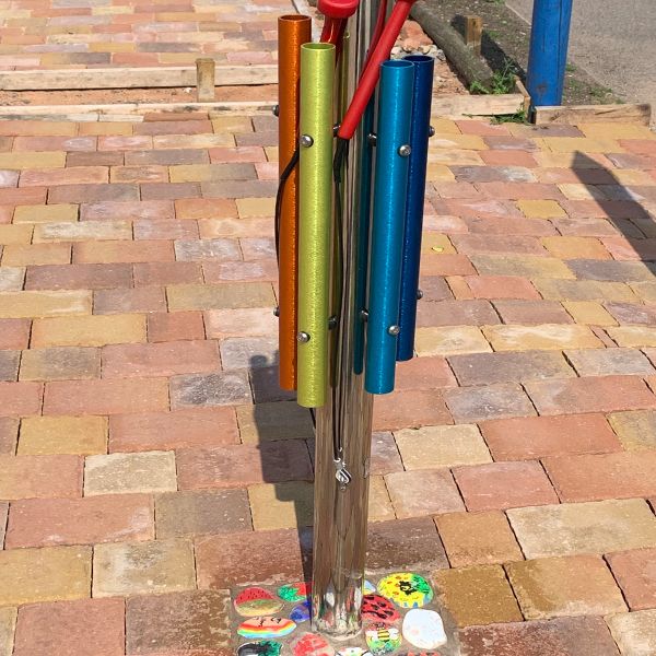 A Rainbow coloured musical chimes post in a musical memorial garden created for a former student