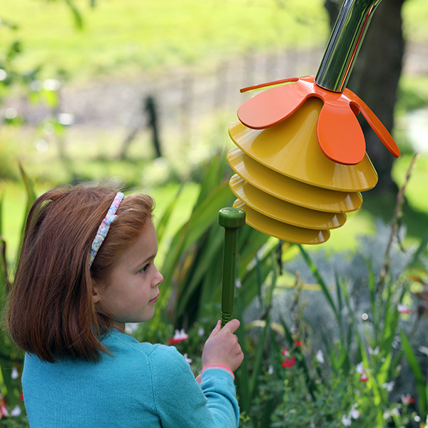 a young girl playing a yellow and orange outdoor musical flower outdoors in a sensory garden