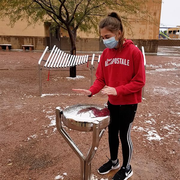 A schoolgirl wearing a red uniform playing an outdoor stainless steel round tongue drum in the school playground