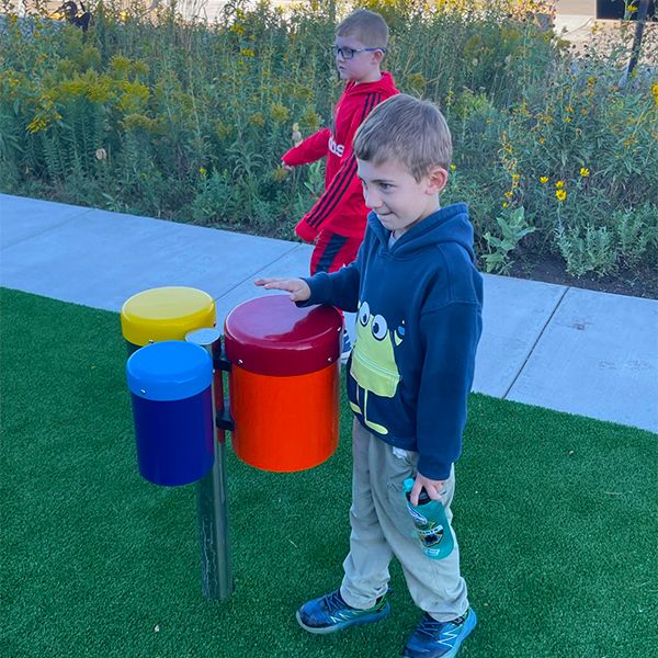 Two young boys playing on a set of outdoor bongo drums in the Kansas Wetlands Center new musical playground