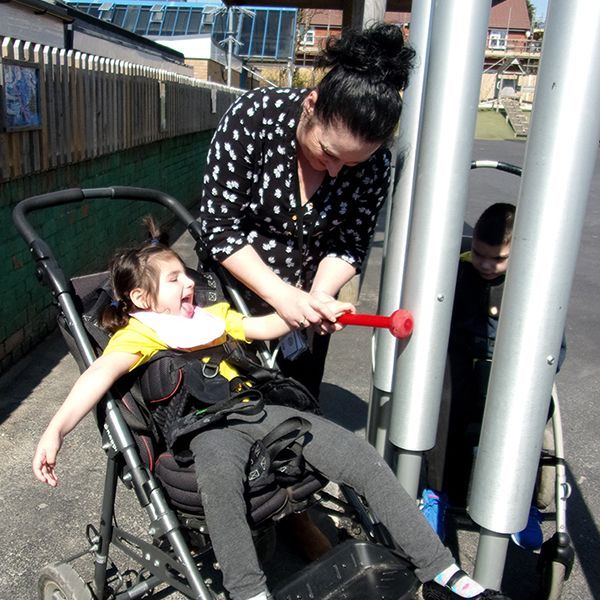 girl with special needs playing a large outdoor chimes with her carer