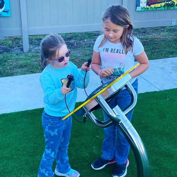 two young girls playing an outdoor drum shaped like a large sunflower in the Kansas Wetlands Center new musical garden