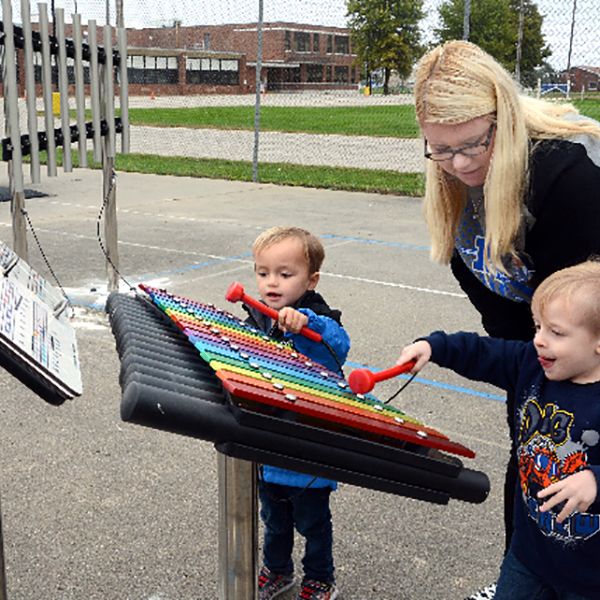 family playing on a rainbow coloured outdoor xylophone and music book in a school playground