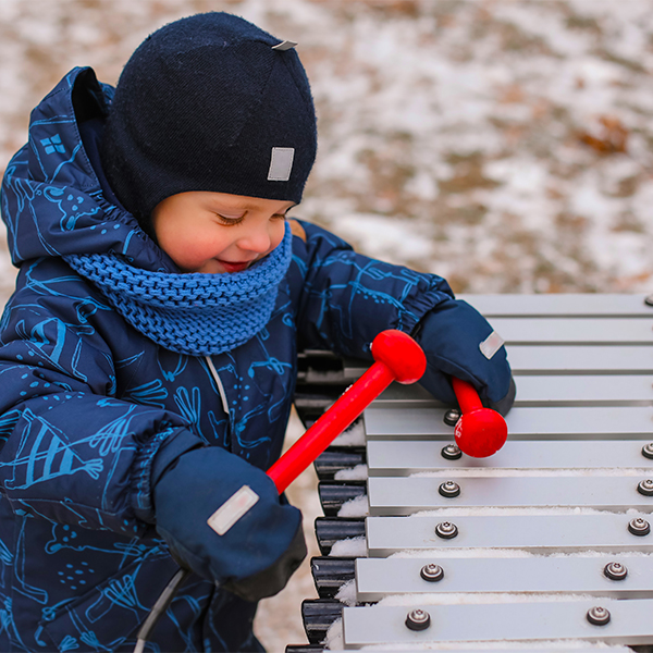 a young boy dressed for cold weather playing on an outdoor xylophone