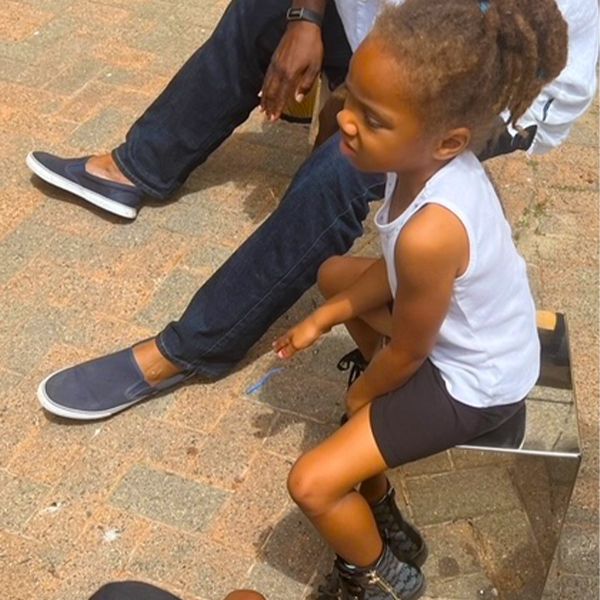 a young black girl sat on top of a silver outdoor cajon drum