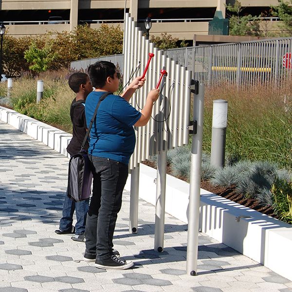 Two young men playing on the silver outdoor musical chimes on the plaza outside White Plains Public Library NY 