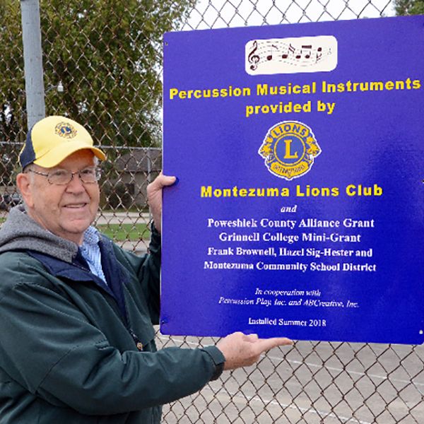 Lions Member stood beside a playground dedication sign in <ontezuma Elementary school