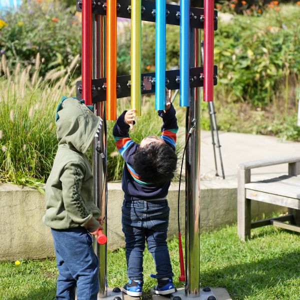 two young boys playing on a a set of small outdoor chimes in a museum sensory garden