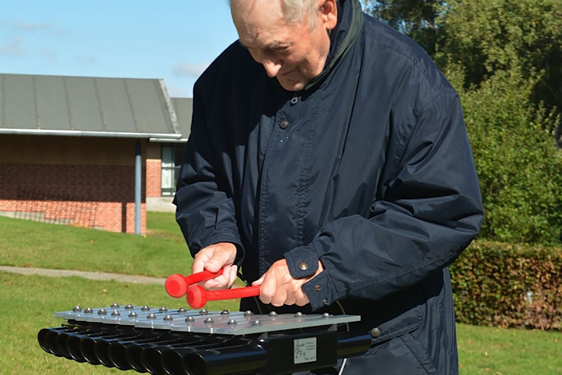 Older man playing an outdoor xylophone in care home garden