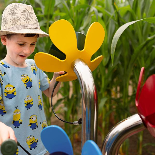 a young boy wearing a hat playing a large outdoor musical instrument shaped like colourful flowers