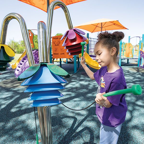 young girl playing outdoor musical chime bells shaped like large colorful flowers