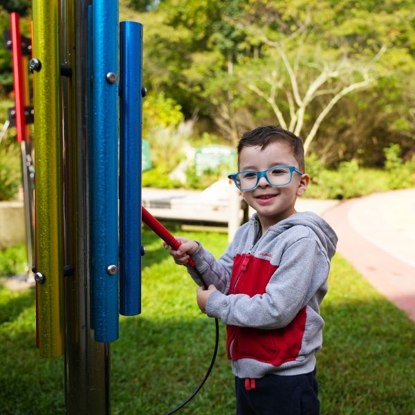 A young boy in glasses playing an rainbow colored outdoor musical chime in a sensory garden