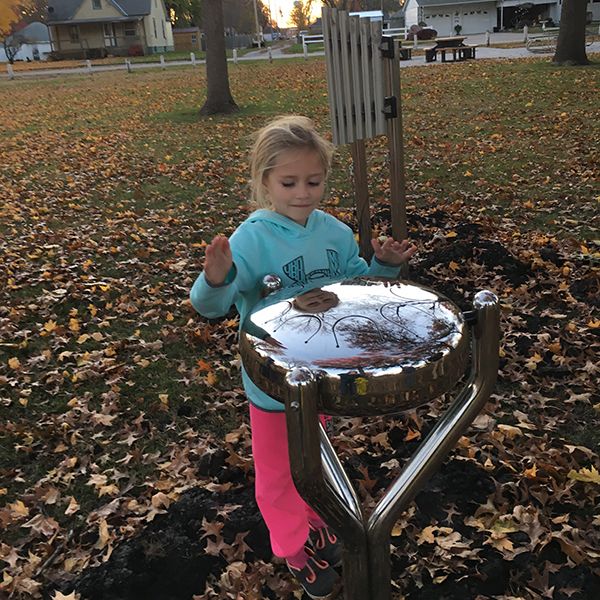 Little girl playing an outdoor steel tongue drum in Anderson Park City of Essex Iowa