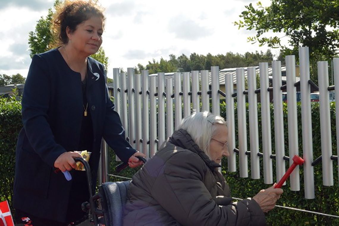 older lady in wheelchair being pushed along while playing on large outdoor chimes