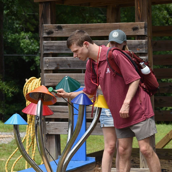 a teenage male playing a large colorful outdoor musical instrument shaped like a crop of field mushrooms