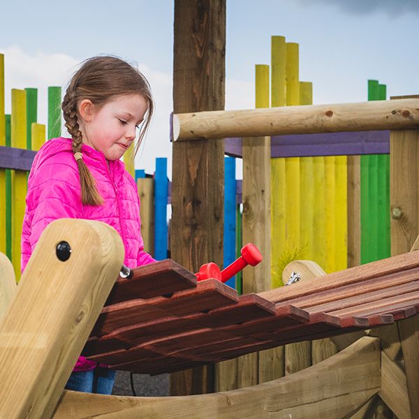 a young girl in a winter coat playing a large wooden outdoor marimba xylophone in the musical maze at the national forest adventure farm