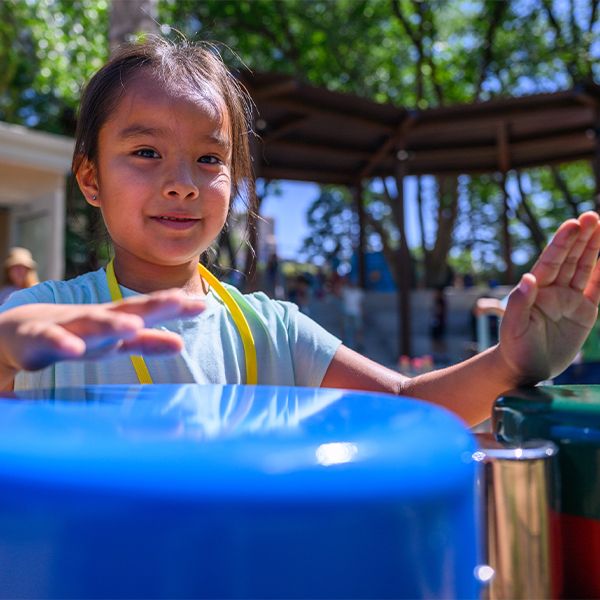 a young girl smiling and playing outdoor drums