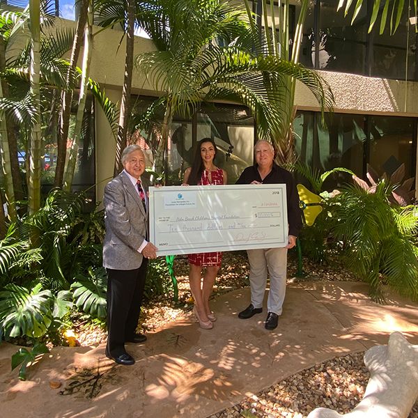 three people holding a large presentation cheque in the dinosaur musical garden at Palm Beach Children's hospital