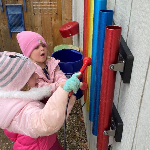 two young girls in winter hats playing rainbow musical chimes hanging on a wall