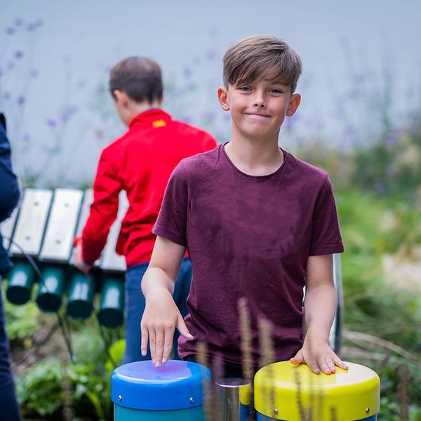 teenage boy plays blue and yellow conga drums in the jess mackie music garden edinburgh children's hospital