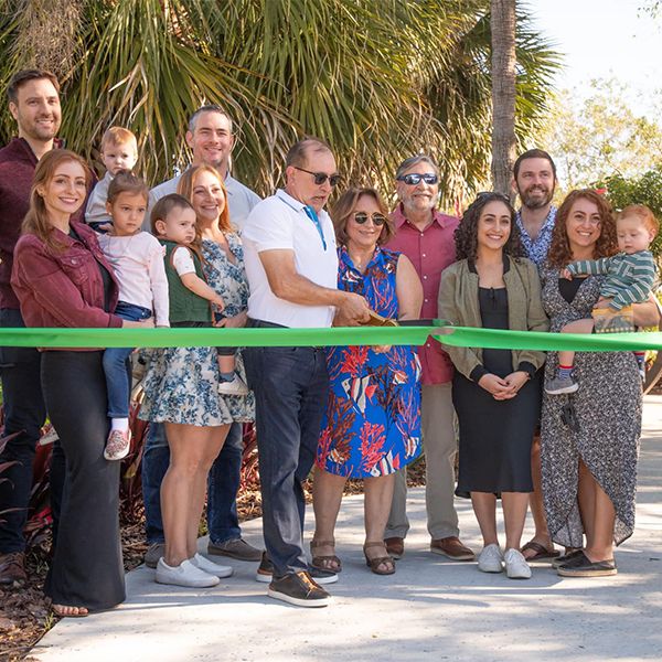 group of adults and children cutting a green ribbon at the opening of the Florida Botanical Gardens new sensory play space