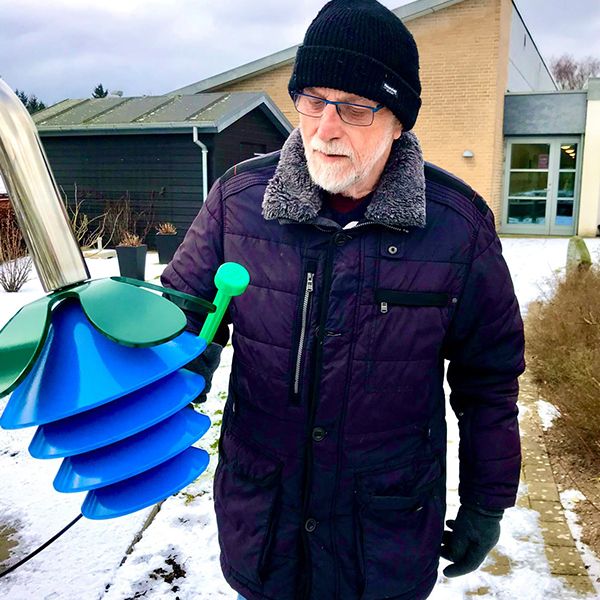 a senior man playing an large outdoor musical instrument shaped like a flower in a music garden in a retirement village