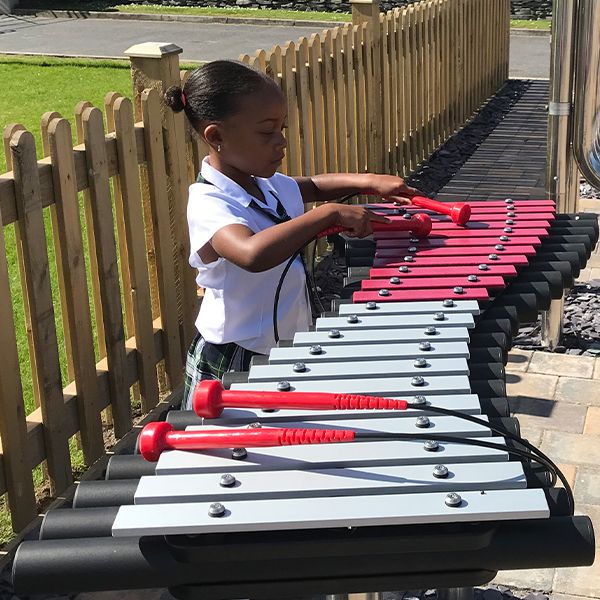 a young black girl playing an outdoor xylophone called a Duo in her school playground