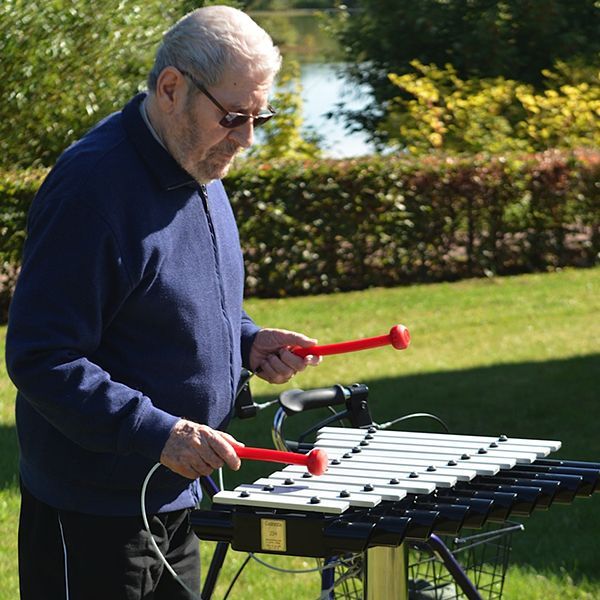 Elderly man in the sun playing on an outdoor xylophone in care home garden