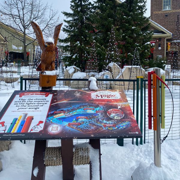 a rainbow colored chimes on a post in front of several unlit Christmas trees