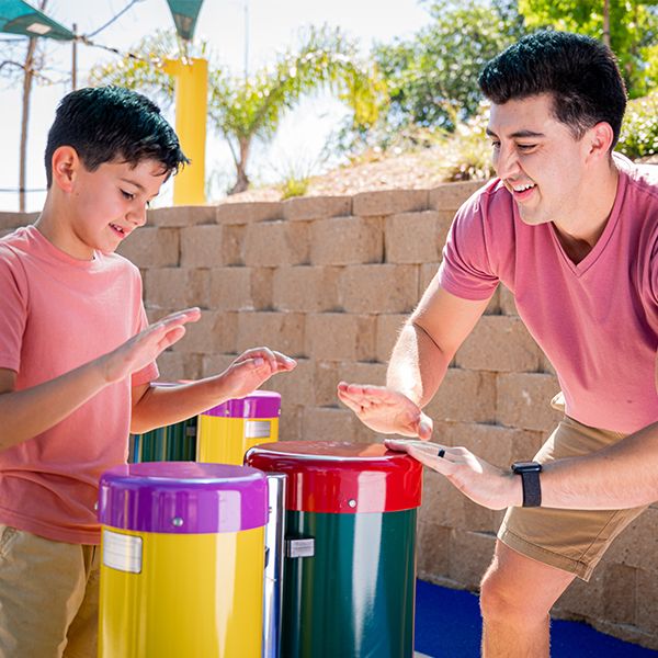 father and young son playing colorful outdoor bongo drums in sesame street music park at seaworld