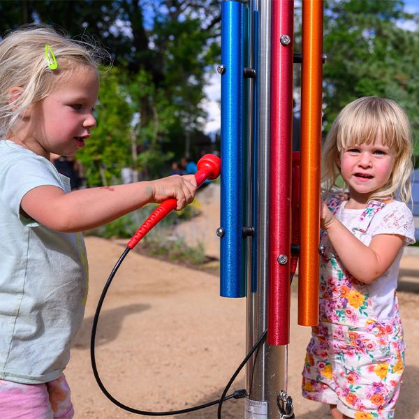 two young girls playing an outdoor musical chime post in a music garden