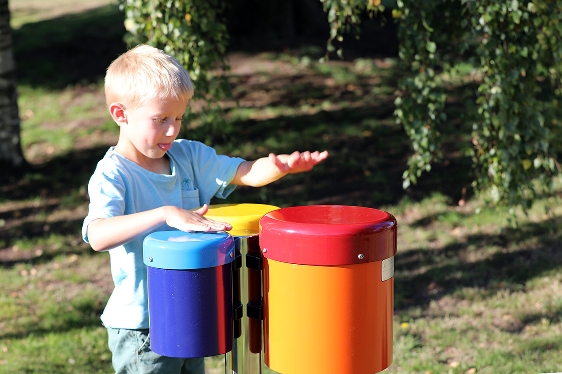 a young boy playing on a set of three colourful outdoor drums in a playground