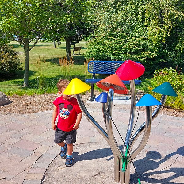 a young boy playing on a large outdoor musical instrument with different colored bells outside benzies shore library