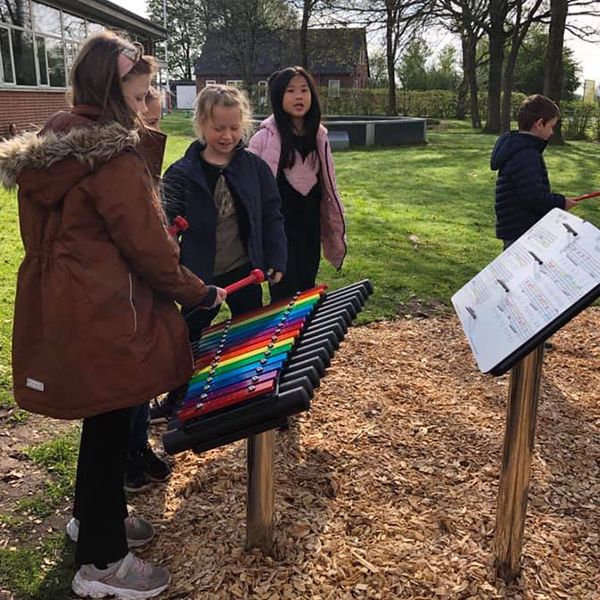 two schoolgirls playing a rainbow coloured outdoor musical instrument in the school playground