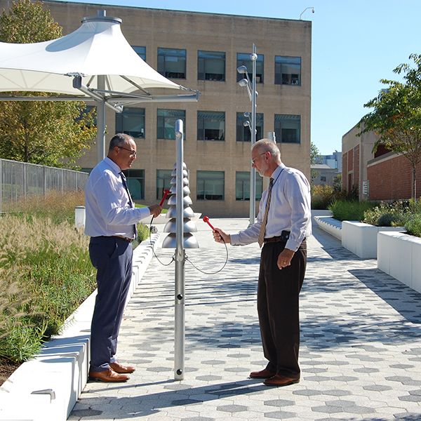 Two men playing on the large silver bell lyre musical instrument on the plaza outside White Plains Public Library NY 