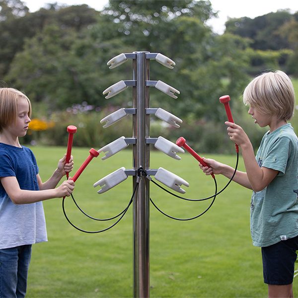 two boys playing an outdoor musical tree with branches made of stone colored temple blocks and with red mallets to hit them with