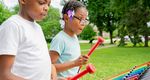 two children playing a large outdoor xylophone in rainbow colors